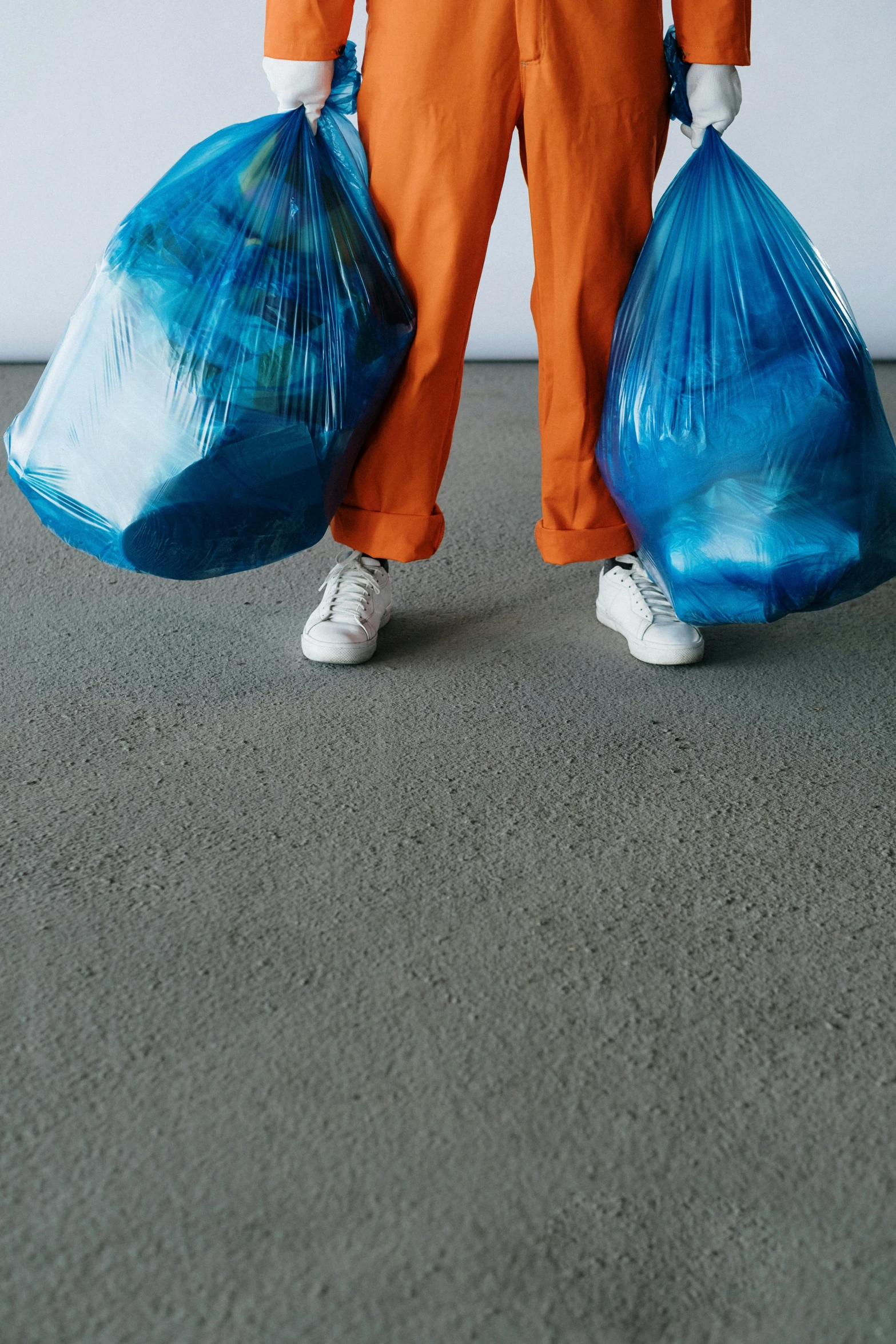 a man in an orange jumpsuit holding two bags of garbage, pexels contest winner, a blue skirt, shiny floors, 2 0 1 0 s, abstract conceptual