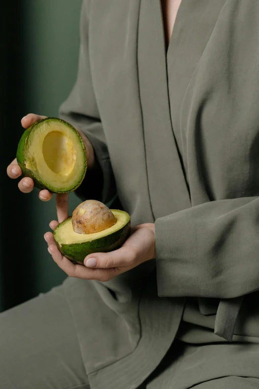 a close up of a person holding an avocado, by Matthias Stom, trending on pexels, hyperrealism, wearing a luxurious silk robe, geometrically realistic, wearing a melon, focus on full - body