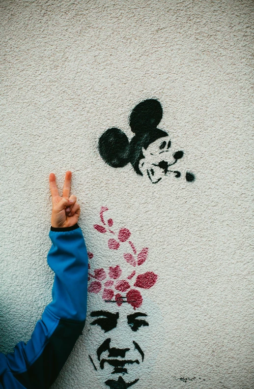 a person standing in front of a wall with a mickey mouse on it, unsplash, peace sign, hand painted, saluting, minnie mouse