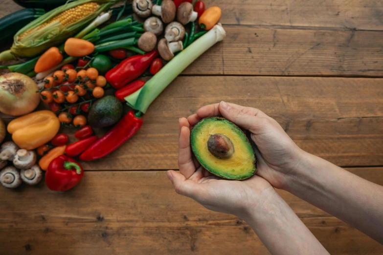 a person holding an avocado in their hands, by Julia Pishtar, trending on pexels, renaissance, vegetables on table and candle, a brightly coloured, on a wooden desk, avatar image