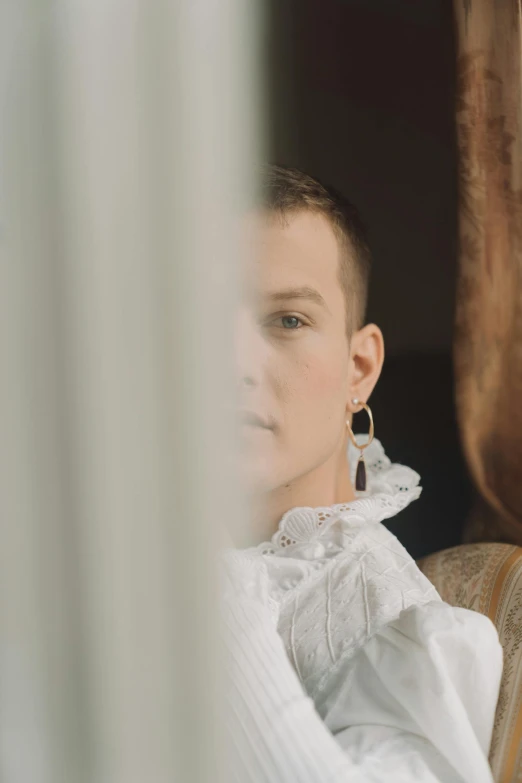 a woman sitting in a chair looking out a window, an album cover, inspired by Anna Füssli, renaissance, silver earring, eleven/millie bobbie brown, wearing pearl earrings, androgynous male