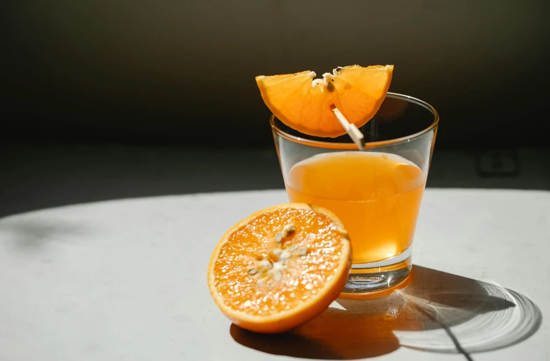 a glass of orange juice sitting on top of a table, pexels, grey orange, background image, syrup, kailee mandel