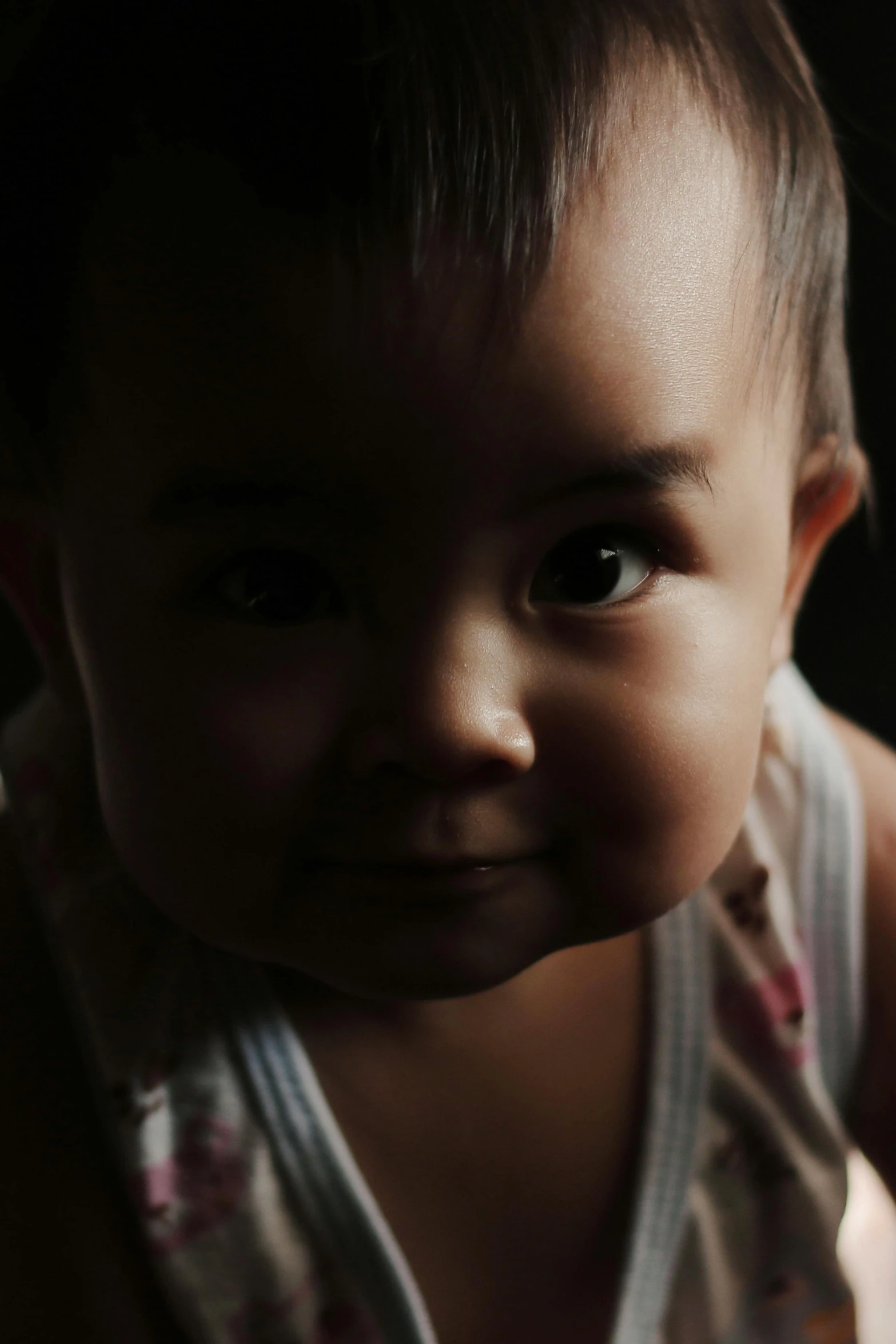 a close up of a baby looking at the camera, by Basuki Abdullah, back light, dimly - lit, portrait shot 8 k, photographed for reuters