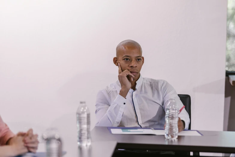 a man in a white shirt sitting at a table, in a meeting room, jemal shabazz, high quality upload, aida muluneh