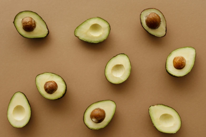 a group of avocados cut in half on a brown surface, by Julia Pishtar, trending on pexels, background image, brass plated, subtle pattern, on a pale background