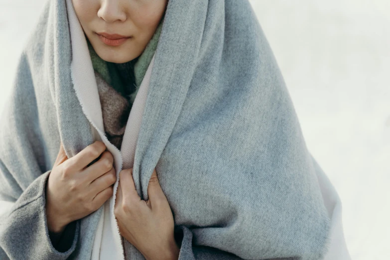 a woman is wrapped up in a blanket, inspired by Goyō Hashiguchi, unsplash, double layer fold over hem, light grey, close shot, coloured