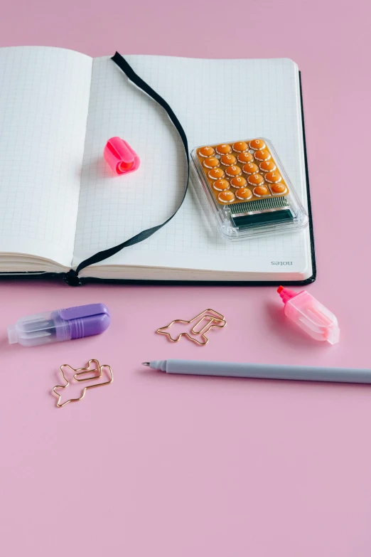 an open notebook sitting on top of a pink surface, a still life, by Julia Pishtar, trending on pexels, made of paperclips, alien capsules, detail shot, detailed product image