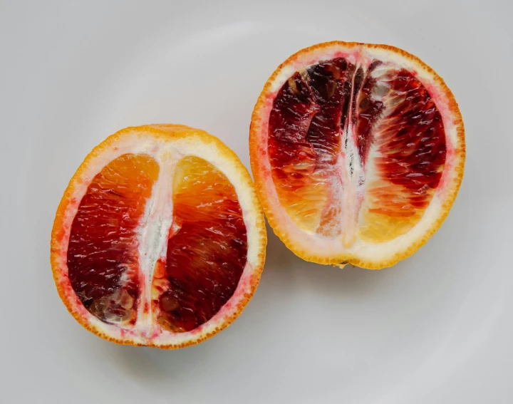 a blood orange cut in half on a white plate, trending on pexels, intense albino, adult pair of twins, bright rim light, purple flesh