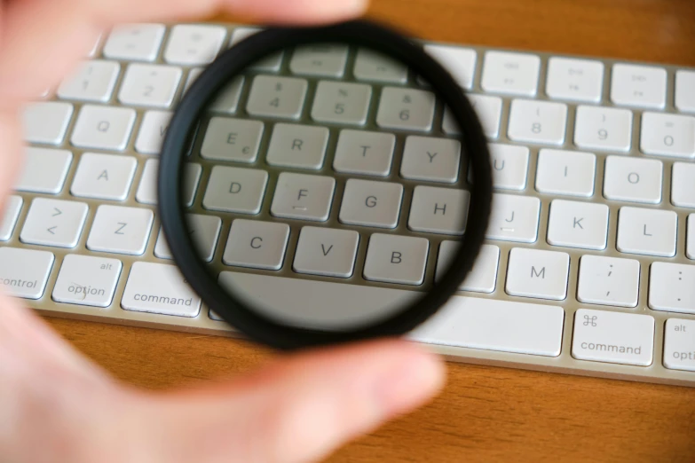 a person holding a magnifying glass over a keyboard, a picture, by Carey Morris, polarizer filter, round-cropped, instagram post, clean photo