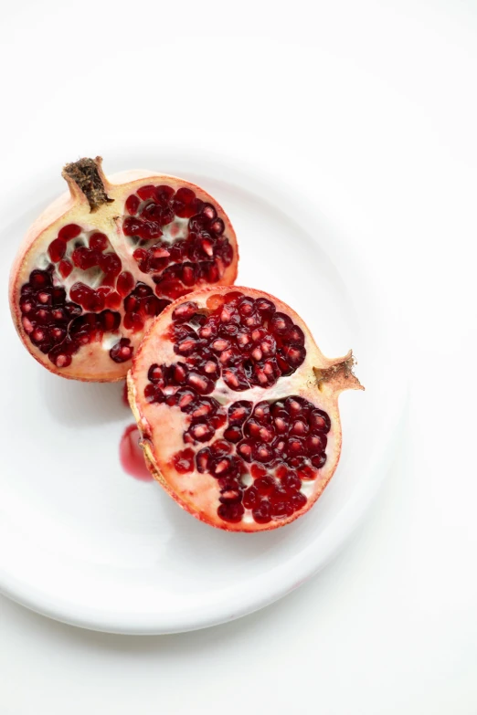 a white plate topped with a cut open pomegranate, trending on unsplash, set against a white background, an olive skinned, yael shelbia, vine