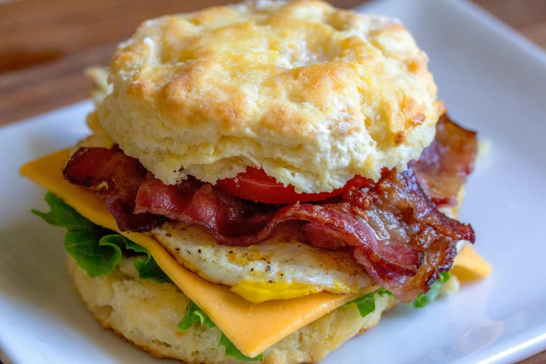 a biscuit sandwich sitting on top of a white plate, by Joe Bowler, pexels, bacon lettuce and tomatos, square, fan favorite, eggs