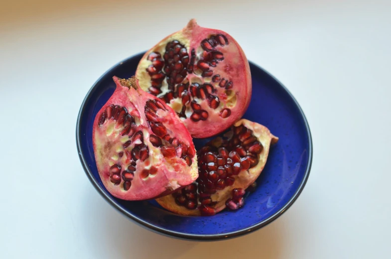 a blue plate topped with pomegranate on top of a white table, pexels, violet polsangi, in a red dish, ash thorp, brown