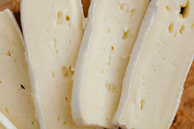 a wooden cutting board topped with slices of cheese, by Jessie Algie, unsplash, art nouveau, soft white rubber, zoomed in, thumbnail, pearlescent skin