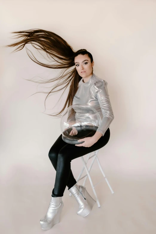 a woman sitting on a chair with her hair blowing in the wind, an album cover, inspired by Julia Pishtar, trending on pexels, silver space suit, sasha grey, studio shoot, dynamic hair movement