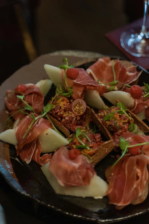 a plate of food on a table with a glass of wine, salami, at night