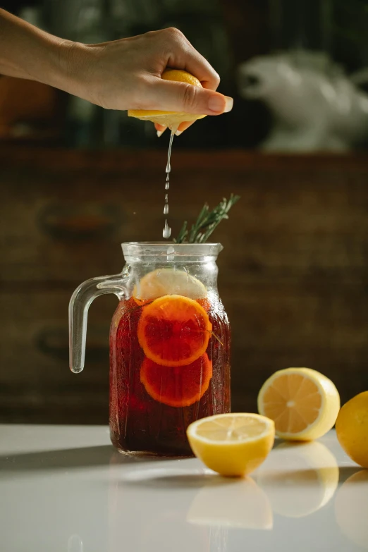 a person squeezing a lemon into a jar, iced tea glass, dark oranges reds and yellows, displayed, item