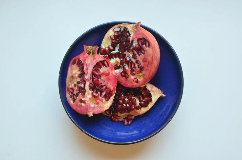 a blue plate topped with a cut open pomegranate, by Carey Morris, pexels, violet polsangi, aged 2 5, seeds, pink