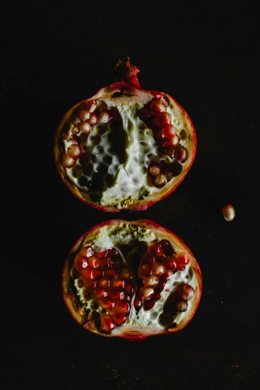 two halves of a pomegranate on a black surface, by Emanuel de Witte, pexels, made of glazed, jen atkin, seeds, 1960s-era