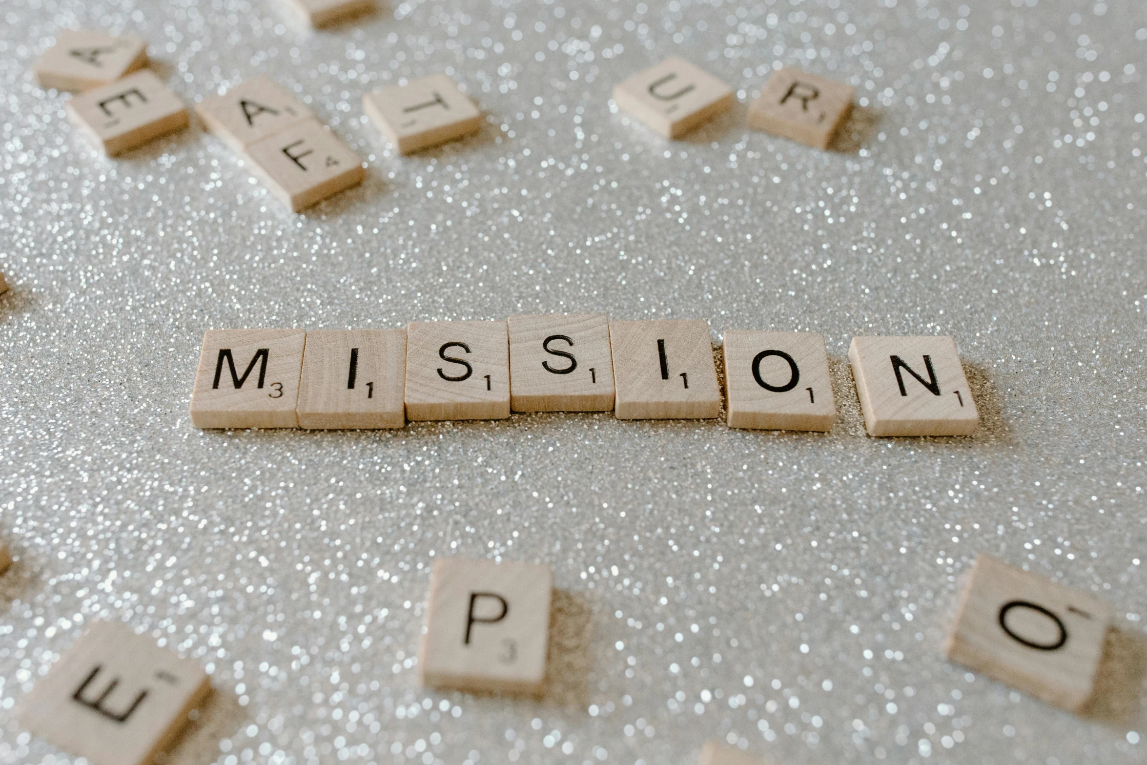 the word mission spelled in scrabbles on a shiny surface, by Alice Mason, unsplash, assemblage, royal commission, a wooden, background image, kneeling and looking up