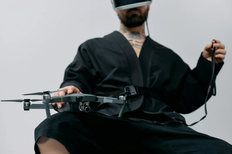 a man in a black robe holding a remote control device, inspired by Kanō Hōgai, unsplash, afrofuturism, floating vr headsets, sitting down, harnesses and garters, hakama kimono