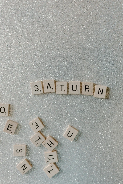 a close up of scrabbles on a refrigerator door, by Sara Saftleven, trending on unsplash, letterism, planet saturn, on a gray background, 🌲🌌