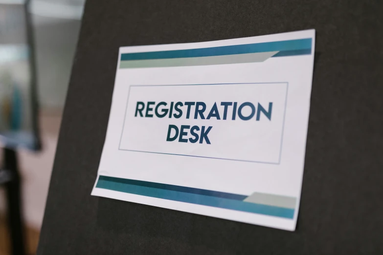 a sign with the words registration desk on it, pexels, process art, sitting on a mocha-colored table, neck zoomed in, colour print, tournament