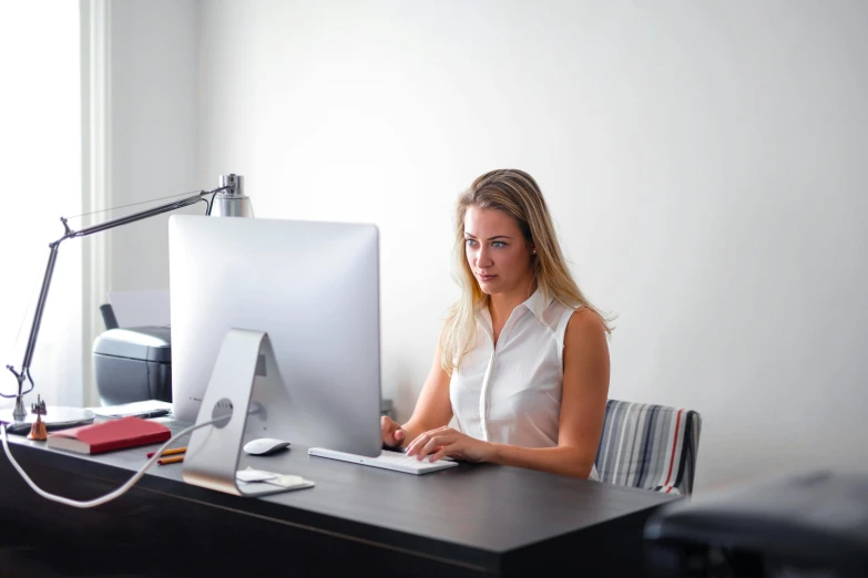 a woman sitting at a desk working on a computer, pexels contest winner, private press, 9 9 designs, white, grey, mid morning lighting