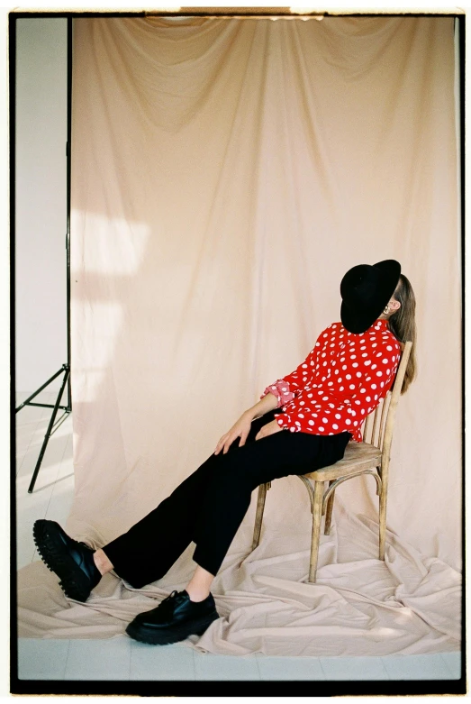 a woman sitting in a chair in front of a white backdrop, by Lucette Barker, trending on pexels, polka dot, red shirt, as fashion editorial 90s, standing in corner of room