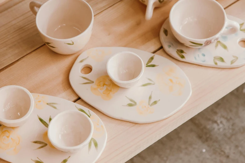 a wooden table topped with cups and saucers, inspired by Annabel Kidston, trending on unsplash, dau-al-set, yellow, handpainted, opal petals, close-up product photo