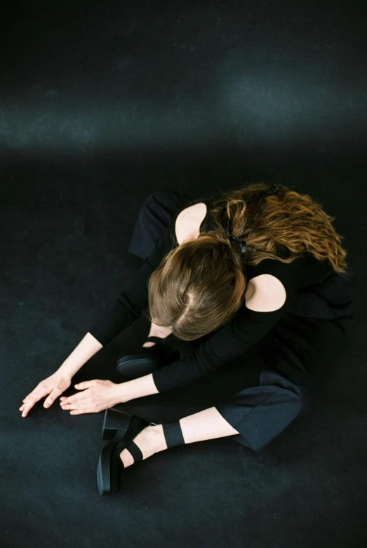 a woman in a black dress sitting on the floor, by Elizabeth Polunin, unsplash, renaissance, hands pressed together in bow, with a hurt expression, studio photo, she is laying on her back