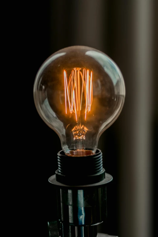 a light bulb sitting on top of a table, dark filaments, warm coloured, iconic design, electric sparks