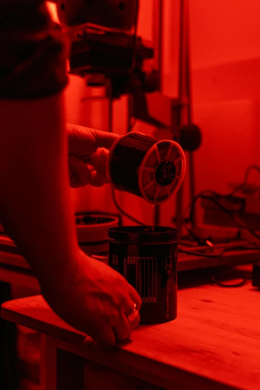 a person pouring something into a can on a table, a silk screen, by Glennray Tutor, unsplash, kinetic art, red laser scanner, in a darkly lit laboratory room, heated coils, black on red