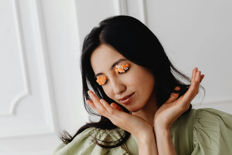 a woman with orange eye patches on her eyes, by Julia Pishtar, trending on pexels, hurufiyya, holding magic flowers, her face in discs, skincare, asian female