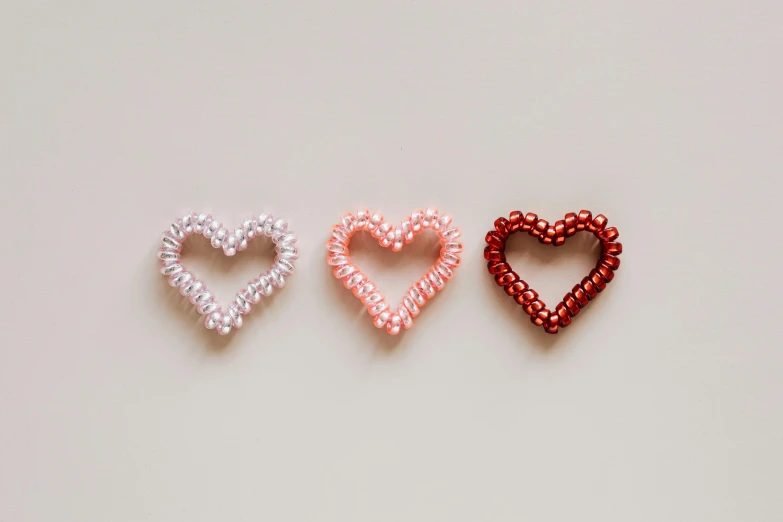 three heart shaped hair clips on a white surface, pexels, beads, thumbnail, rgb, 3