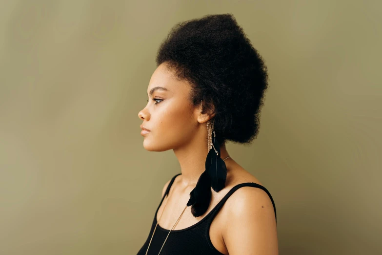 a close up of a person wearing a necklace and earrings, an album cover, trending on pexels, hurufiyya, raven hair, side profile centered portrait, plain background, big hair