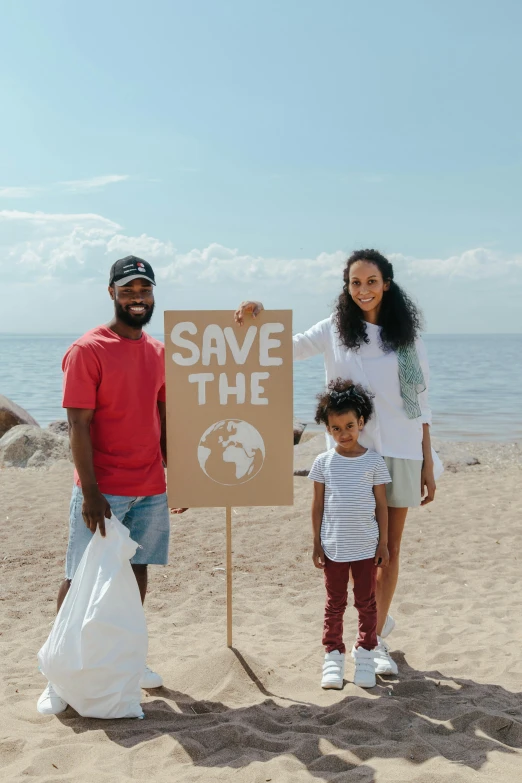 a group of people standing on top of a sandy beach, eco-friendly theme, of a family standing in a park, promo image, woman holding sign