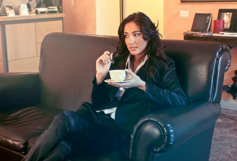 a woman sitting on a couch with a cup of coffee, by Giuseppe Avanzi, pexels, renaissance, young arab monica bellucci, office clothes, cigar, having a snack