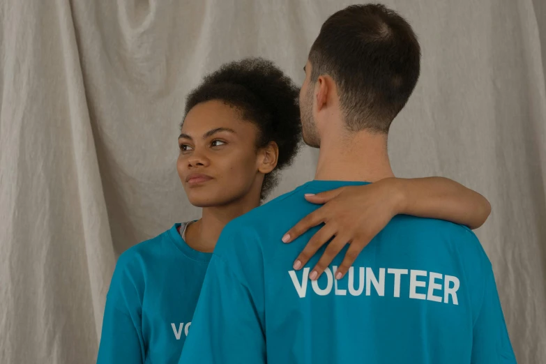 a man and a woman wearing volunteer shirts, by Matija Jama, pexels contest winner, cyan, looking her shoulder, embracing, low quality photo
