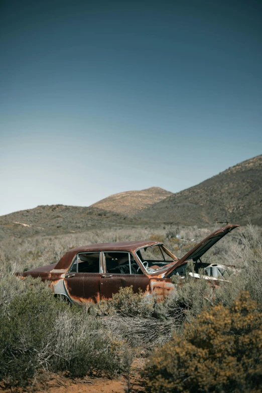 an old rusted car in the middle of the desert, pexels contest winner, in a valley, late 1 9 6 0's, three-quarter body, side