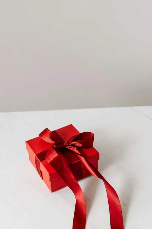 a red gift box sitting on top of a white table, by Luma Rouge, on a gray background, small, 7, ribbon