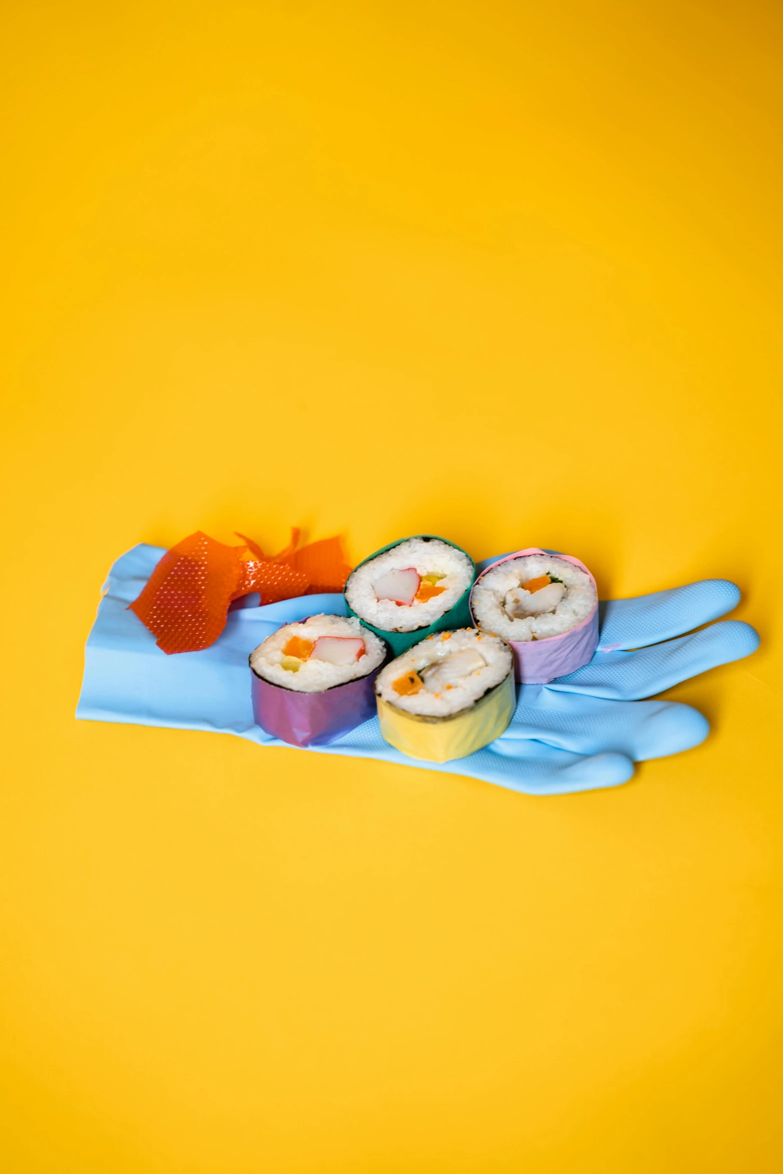 a pair of gloves holding sushi on a yellow background, unsplash, mingei, colorful plastic, blue gloves, fujifilm”