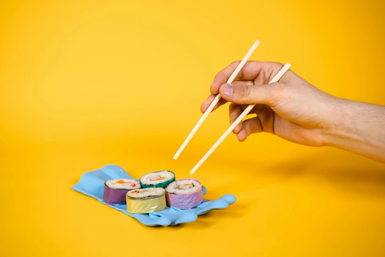 a person holding chopsticks over a plate of sushi, inspired by Maki Haku, plasticien, blue and yellow theme, cardboard, pastel colours, 6 pack