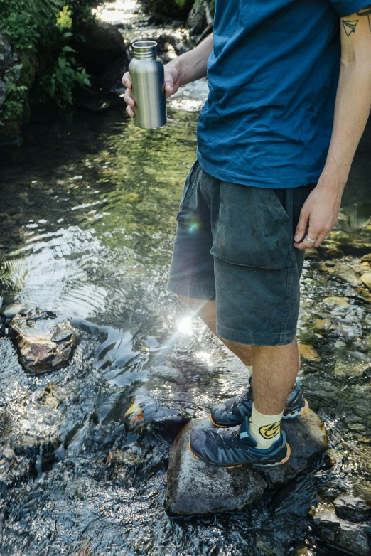 a man standing on a rock in a stream, gray shorts and black socks, tardigrade wearing sunglasses, water reflecting suns light, hydration