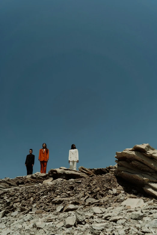 a group of people standing on top of a rocky hill, an album cover, unsplash, minimalism, three women, cinematic outfit photo, abandoned on mars, uniform off - white sky