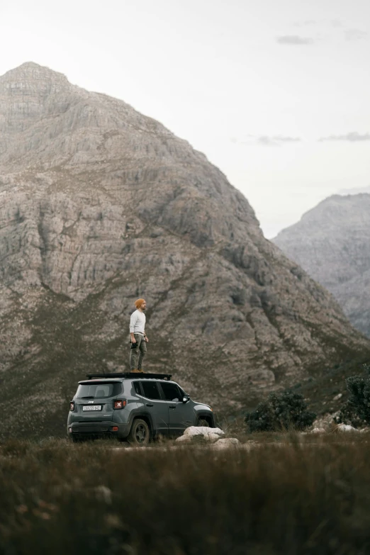 a man standing on top of a car in front of a mountain, by Jessie Algie, trending on unsplash, conceptual art, jeep, tall thin, flat lay, a creature 5 meters tall