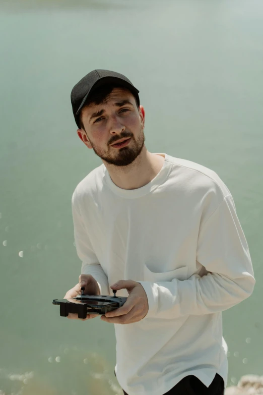 a man standing next to a body of water holding a cell phone, discord profile picture, mark edward fischbach, holding controller, an all white human