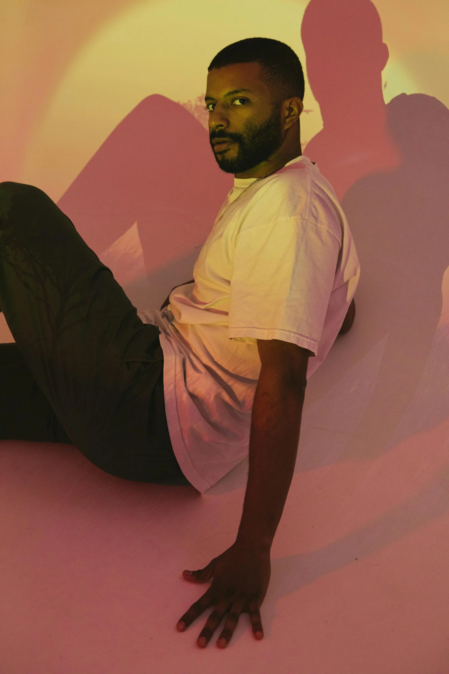 a man sitting on top of a pink floor, an album cover, inspired by Paul Georges, dynamic pose, bearded, ( ( dark skin ) ), grayish