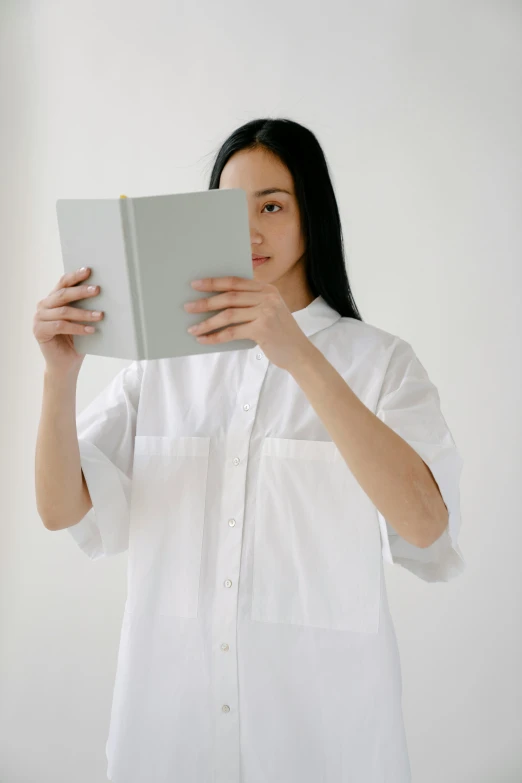 a woman holding a book in front of her face, by helen huang, wearing a white button up shirt, off - white collection, kiko mizuhara, white space