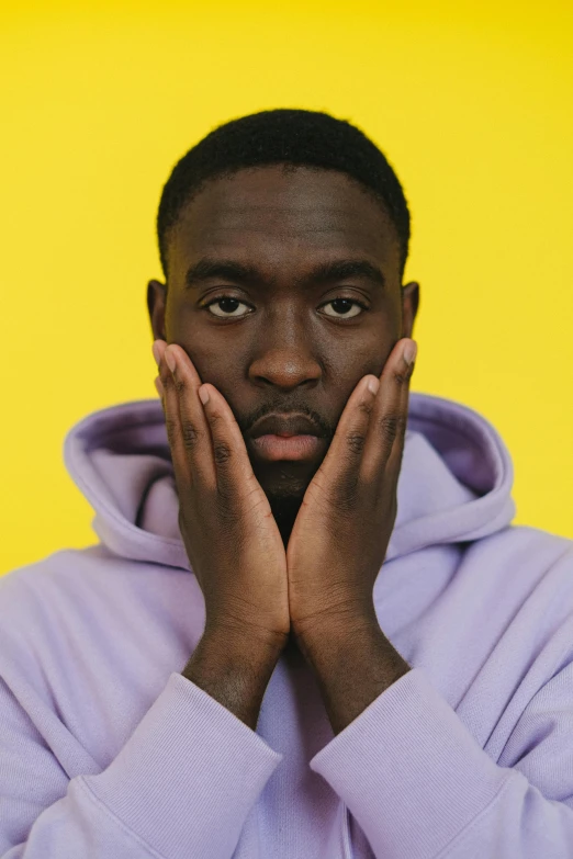 a man in a purple hoodie covers his face with his hands, trending on pexels, adut akech, sleek yellow eyes, pastels, jaylen brown