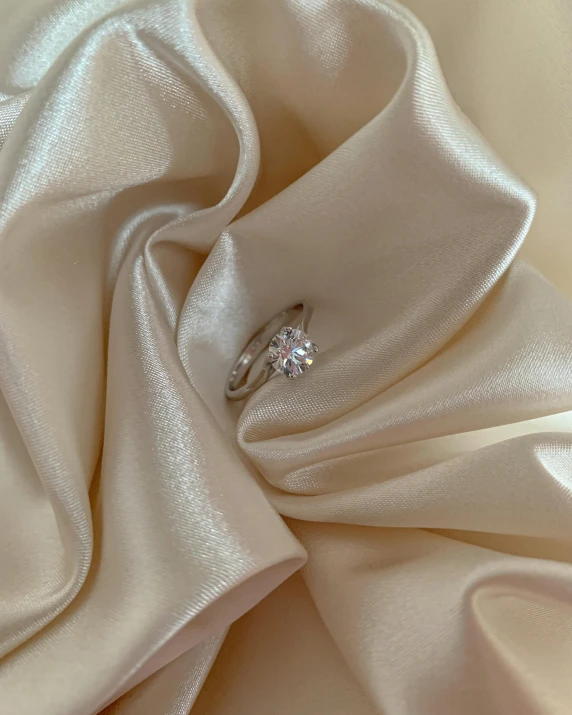 a diamond ring sitting on top of a white cloth, by Emma Andijewska, pexels contest winner, photorealism, thumbnail, 15081959 21121991 01012000 4k, lit from above, beautiful flowing fabric